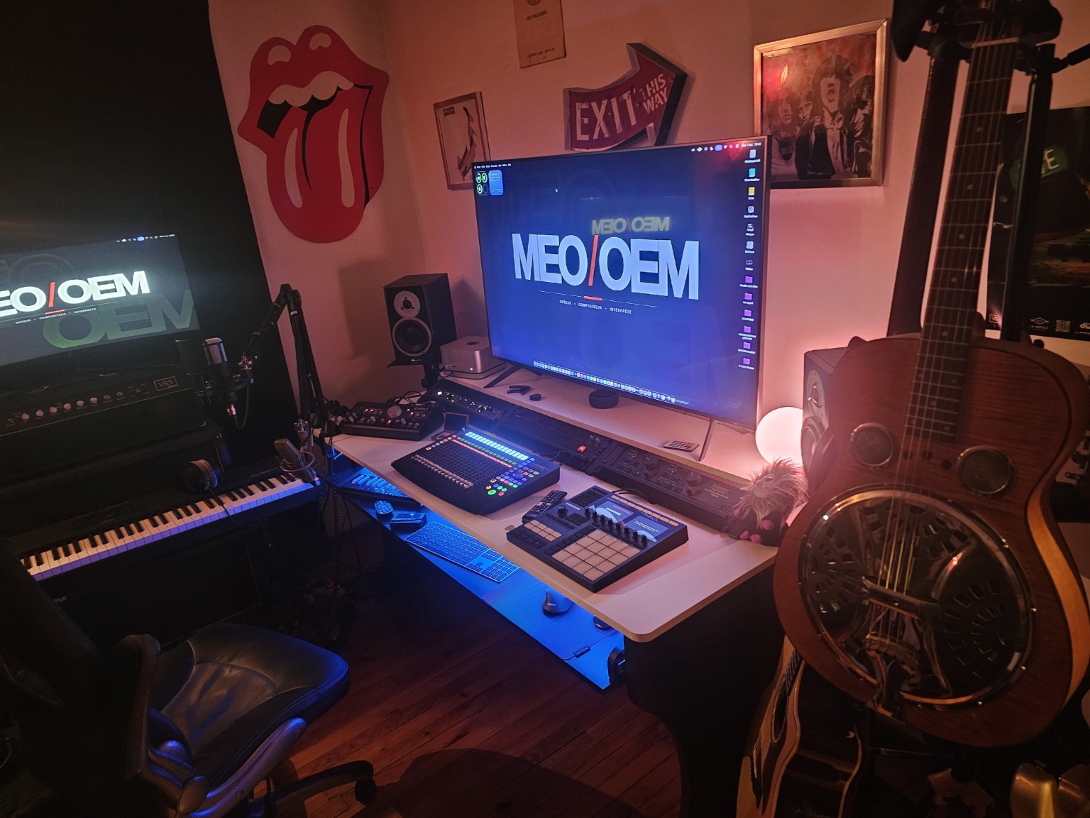 Le poste de travail du studio MEO / OEM, ses claviers et ses guitares dans une ambiance rouge et bleue.